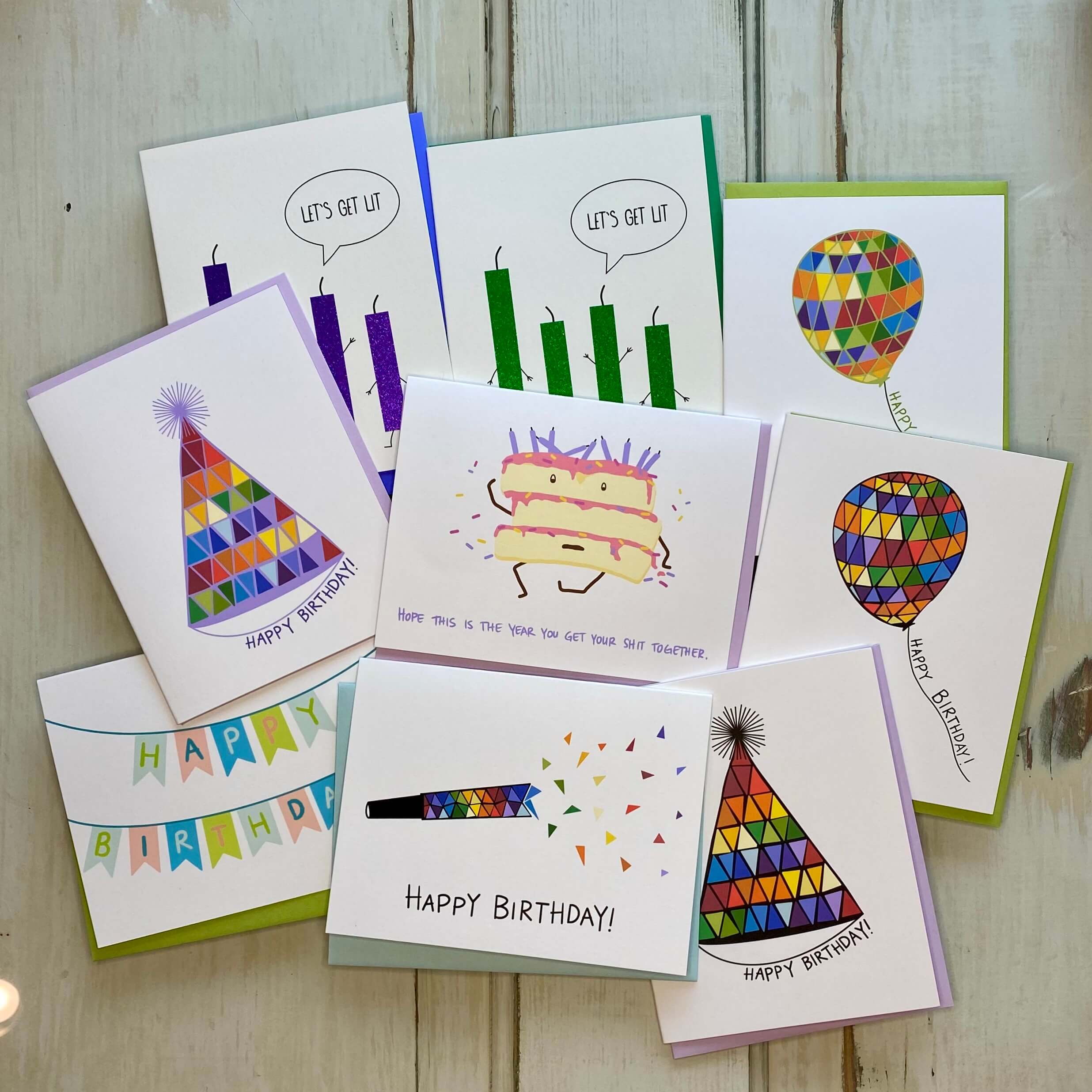 Collection of birthday cards with bright, rainbow designs, against a white wood background