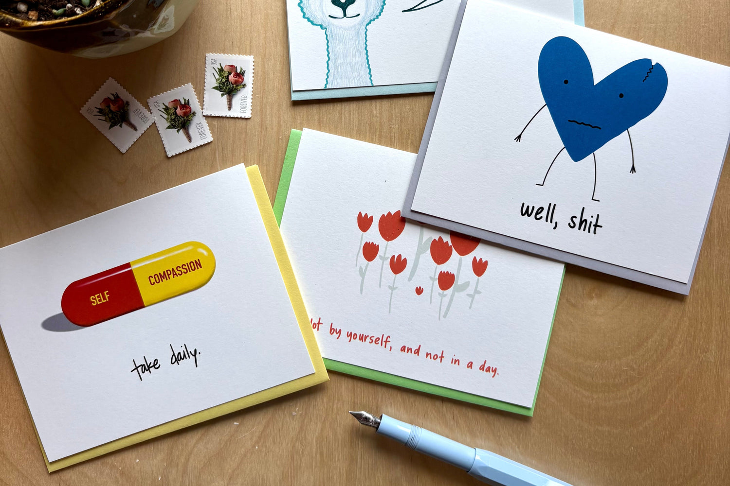 Collection of encouraging greeting cards on a table with stamps and a pen.