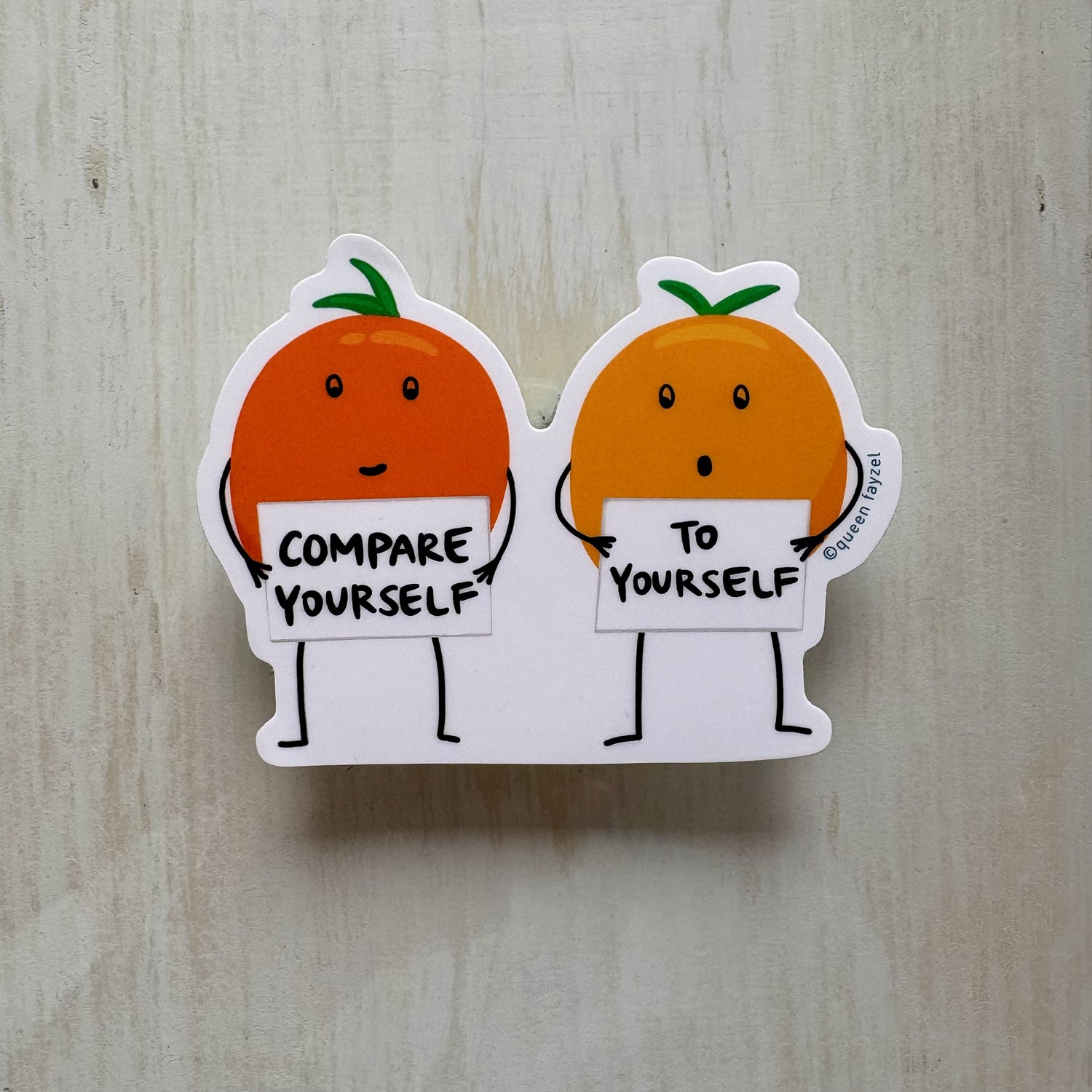 Two cartoon oranges holding signs with motivational text on a wooden surface