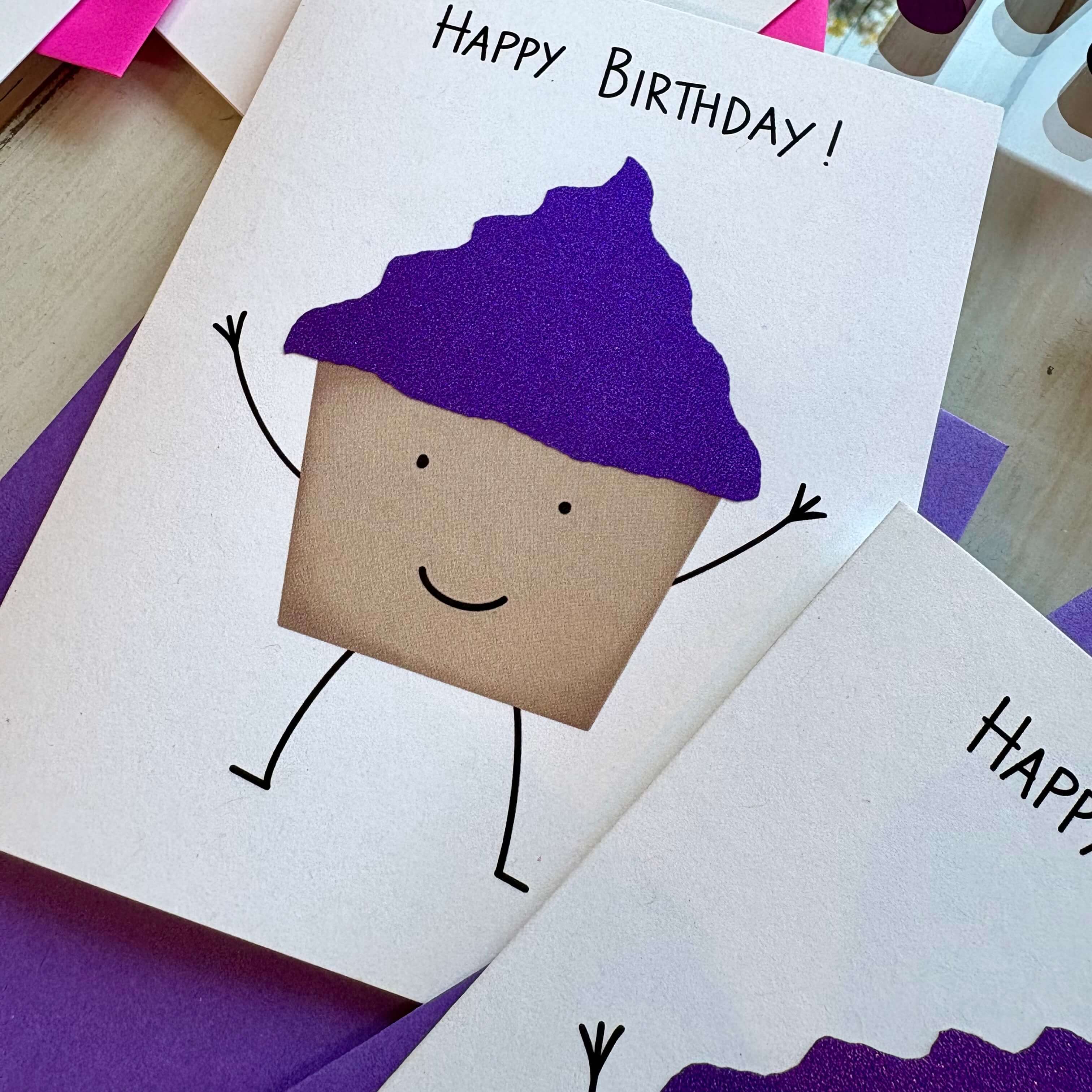 Birthday card with cupcake character wearing purple glitter frosting on a wooden table
