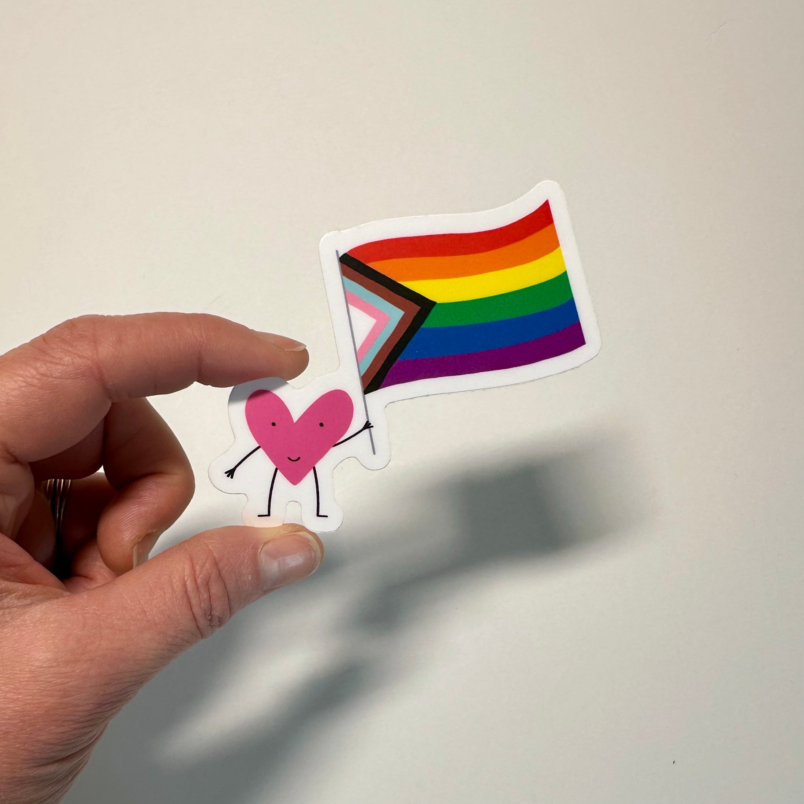 Hand holding a sticker with a rainbow flag and heart design on a plain background