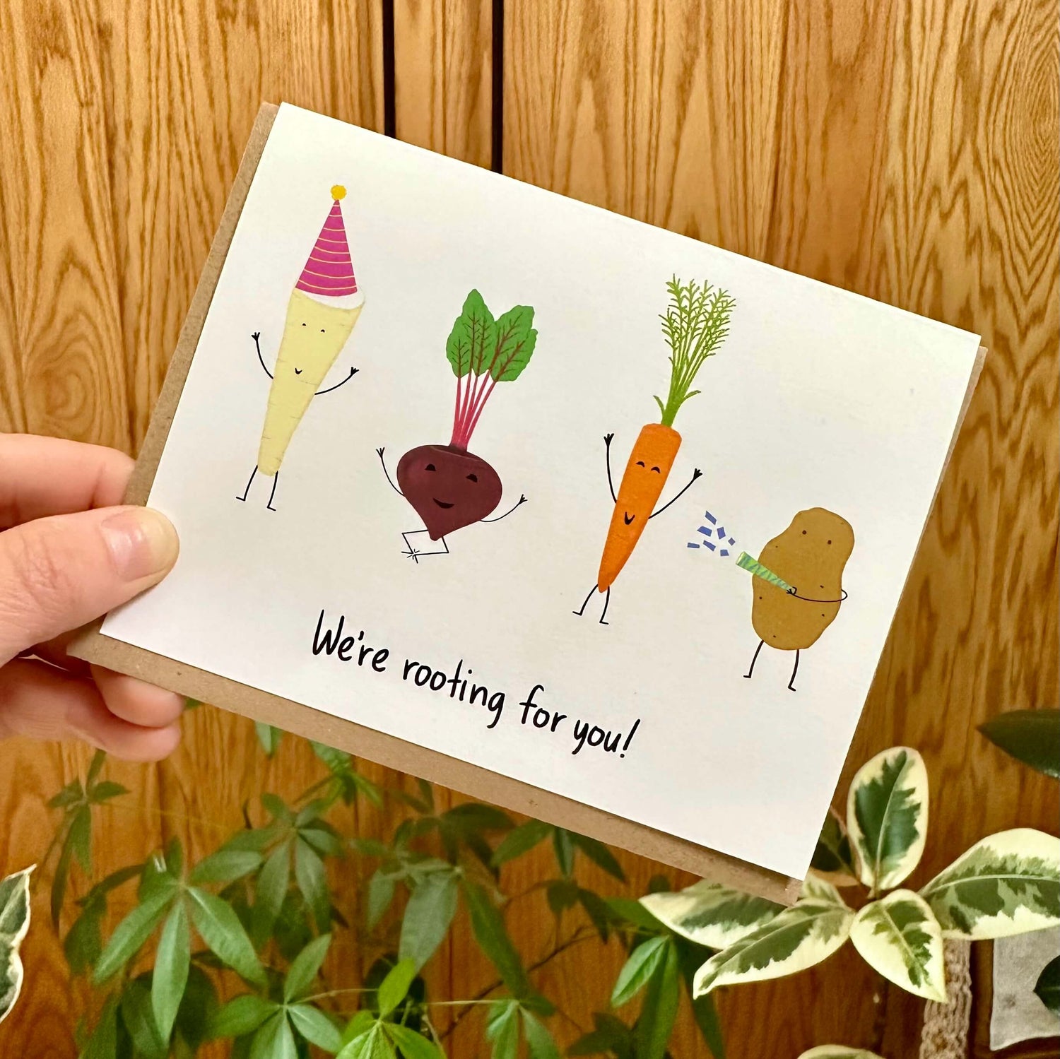 Hand holding the edge of an encouragement card with four festive root vegetables and text &quot;we&