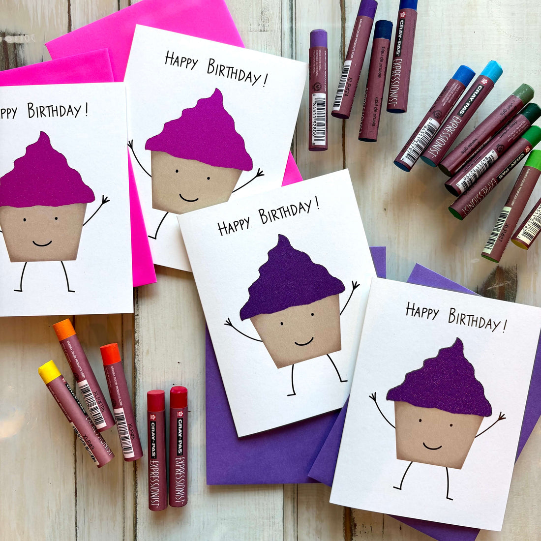 pink and purple glitter cupcake birthday cards scattered on a table with oil pastels.