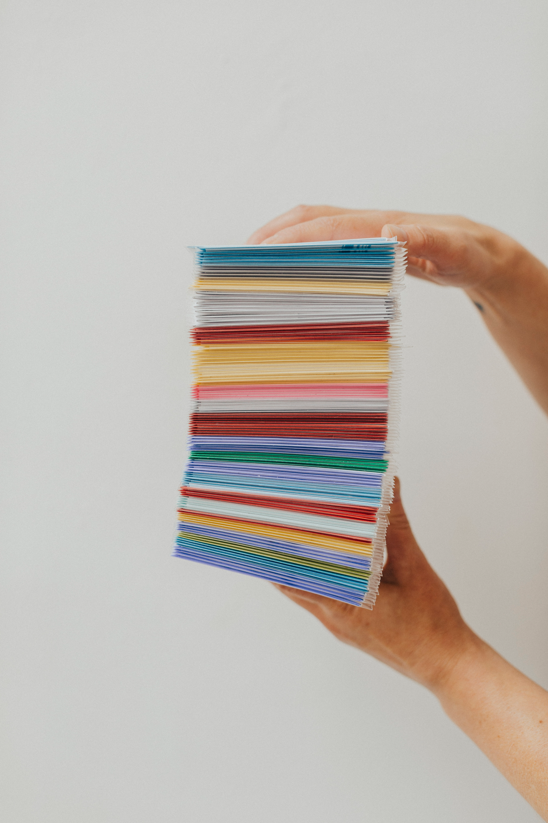 Two hands holding a stack of colorful greeting cards.