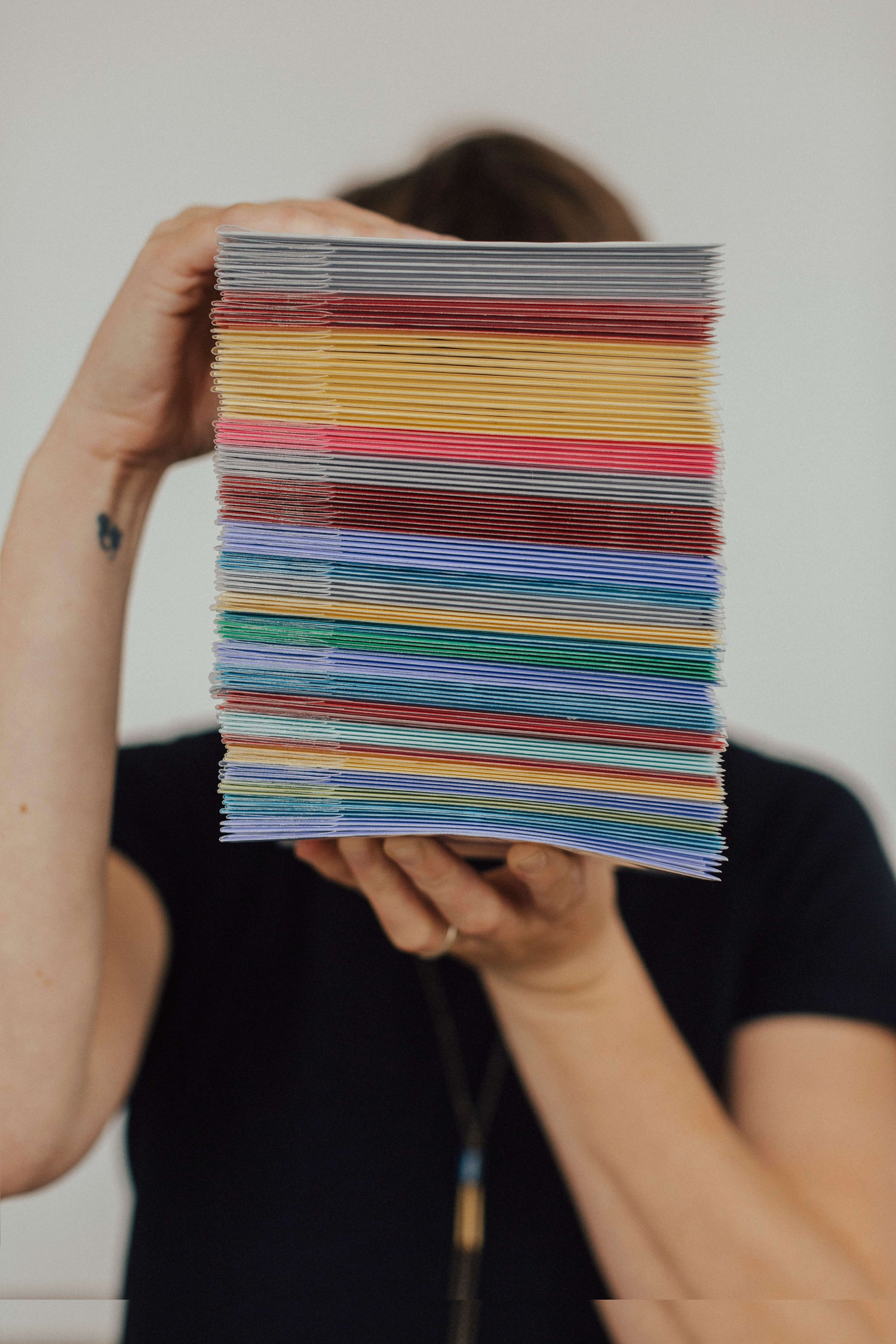 Two hands holding a tall vertical stack of greeting cards with different brightly colored envelopes.