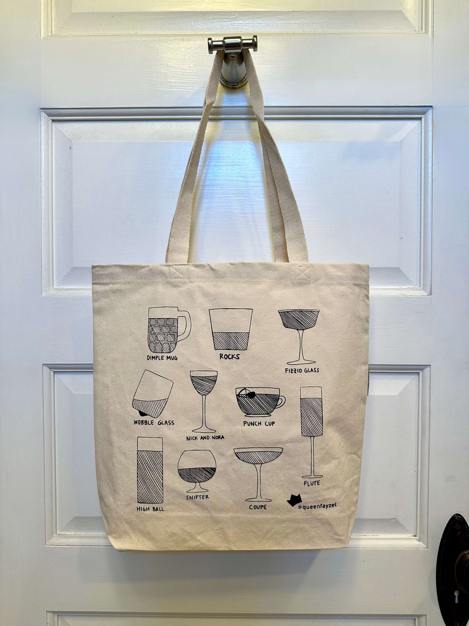 tote bag printed with different drinkware hanging on a hook against a white door