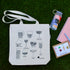canvas tote bag with drinkware design arranged in grass with a water bottle, notebook, pen, and set of greeting cards