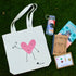 cute tote bag with waving heart design laid out on grass with a water bottle, journal, book, and set of greeting cards