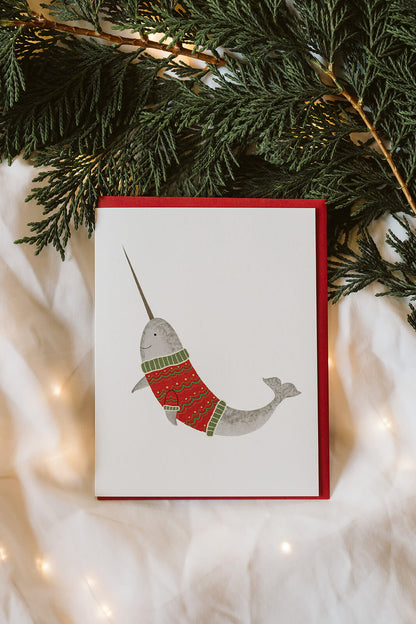 simple Christmas greeting card of a smiling narwhal wearing a red and green holiday sweater
