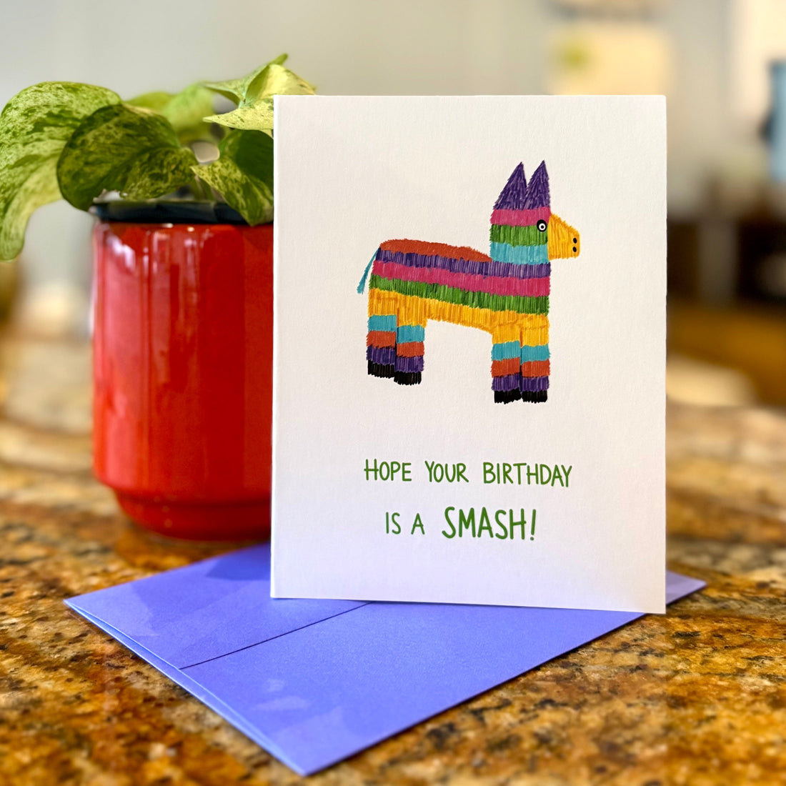 Birthday card with colorful llama pinata design and purple envelope on a table.