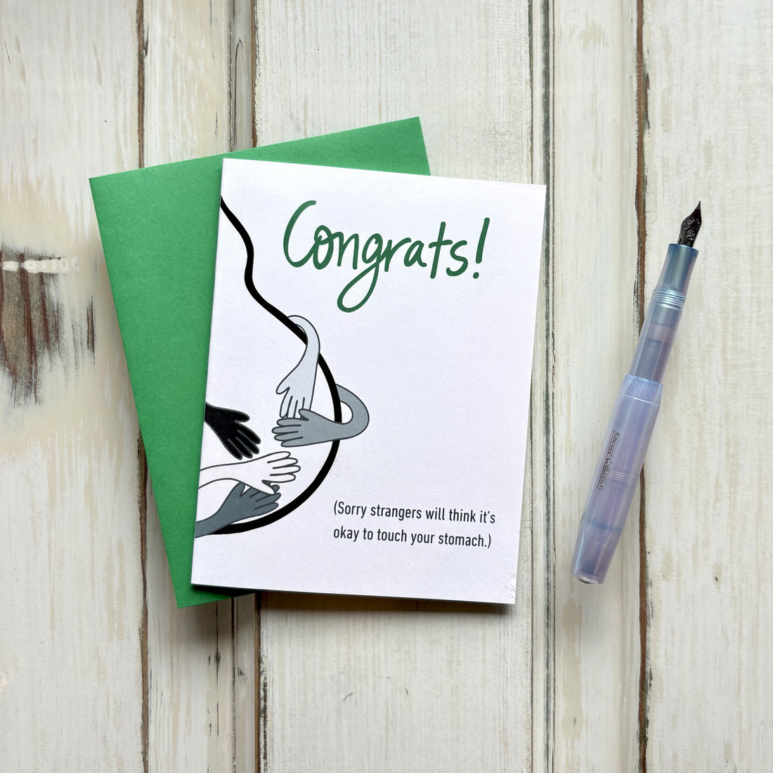 Funny pregnancy congrats card on a wooden table showing a belly silhouette touched by multiple hands, captioned "Congrats! (Sorry strangers will think it&
