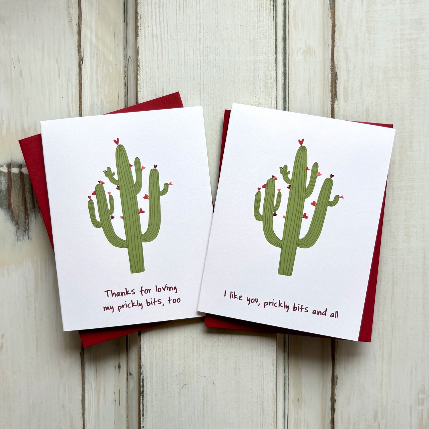 Two cute valentine love cards with a green cactus with red heart flowers, paired with red envelopes against a wooden background.