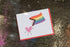 greeting card celebrating the queer community with a smiling heart waving a progress pride flag