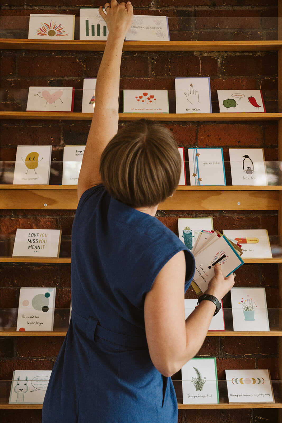 Faye of Queen Fayzel reaching for a greeting card on a shelf