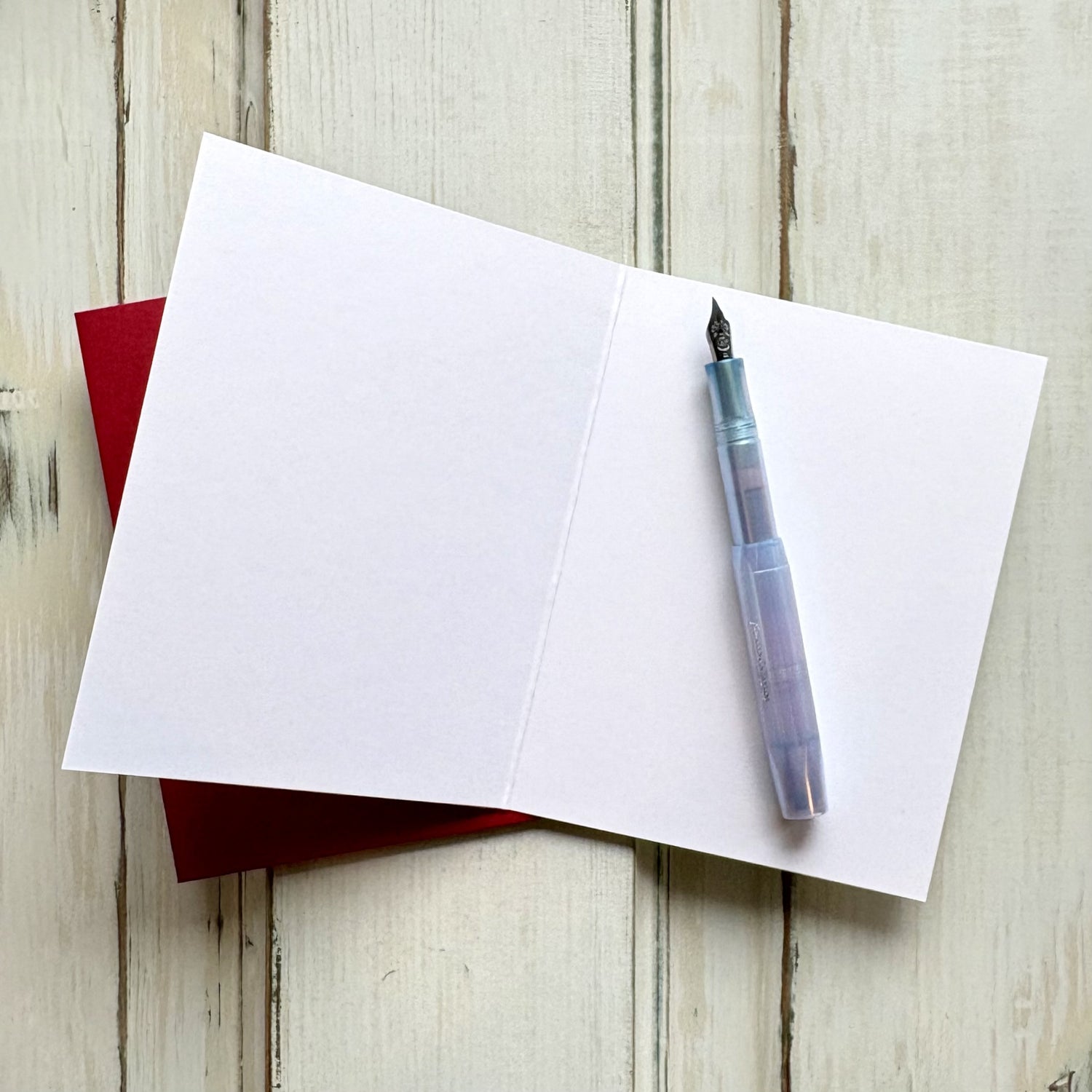 An open, blank greeting card on top of a red envelope, with a fountain pen resting on the card.