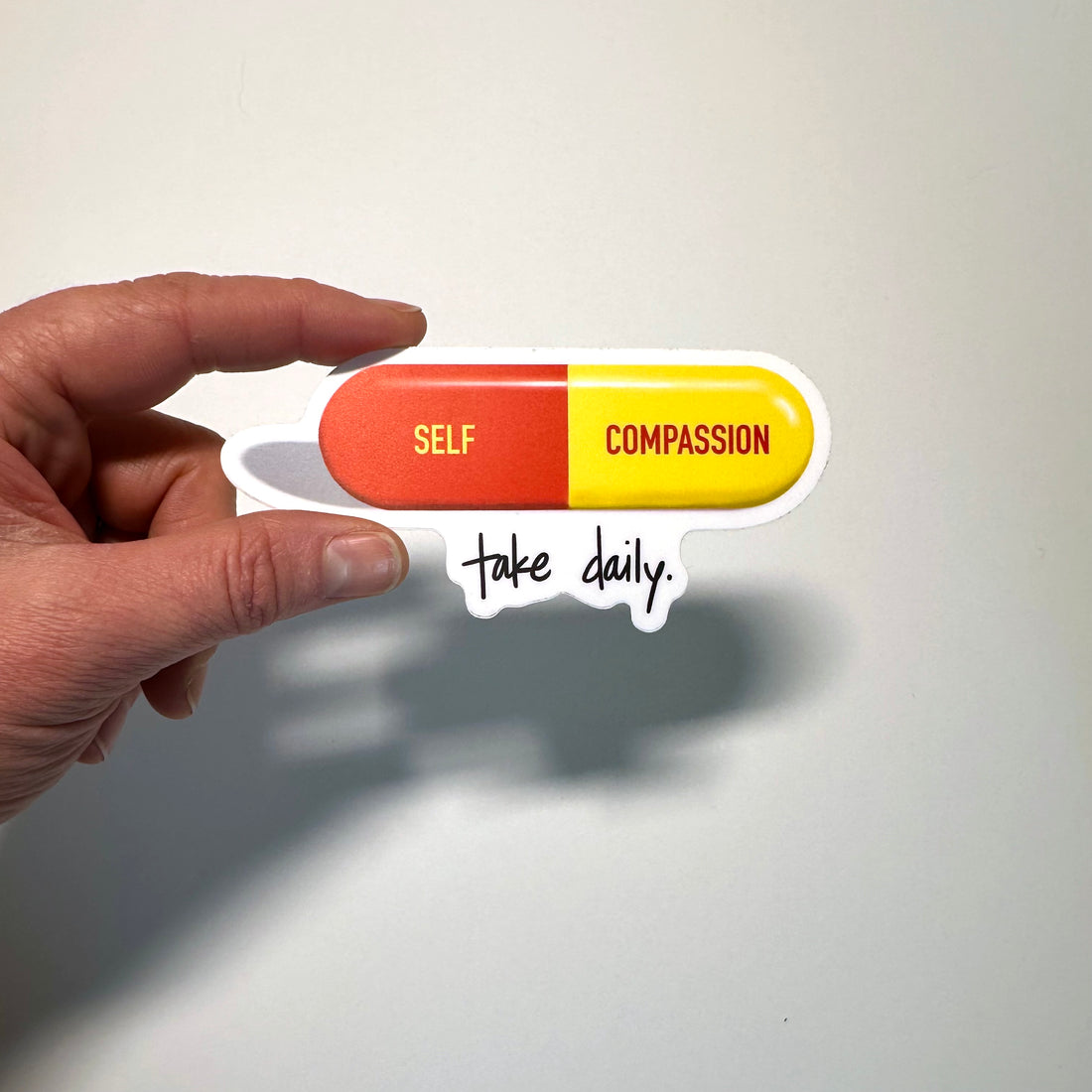 Hand holding a pill-shaped sticker with &