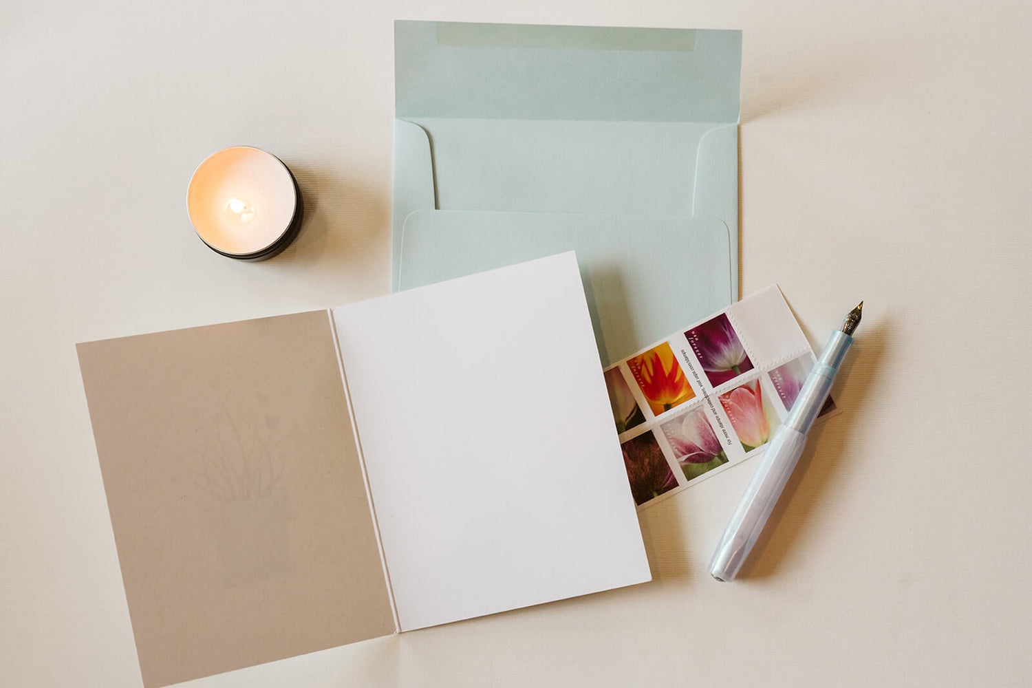 open greeting card with a light blue envelope. a fountain pen and stamps are in the background.