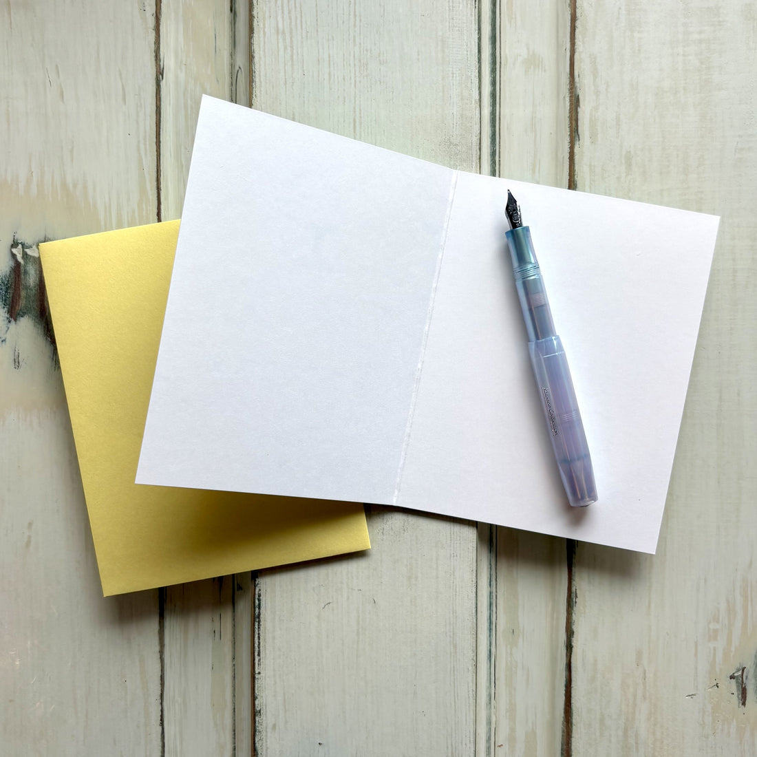 Fountain pen on an open blank greeting card with a yellow envelope