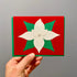 Holiday greeting card with red cardstock, a handmade, white, layered poinsettia flower with gold glitter center and green leaves.