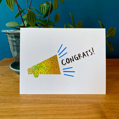 Congratulations card with a sparkly gold bullhorn and the text "Congrats!" The card has a matching blue envelope