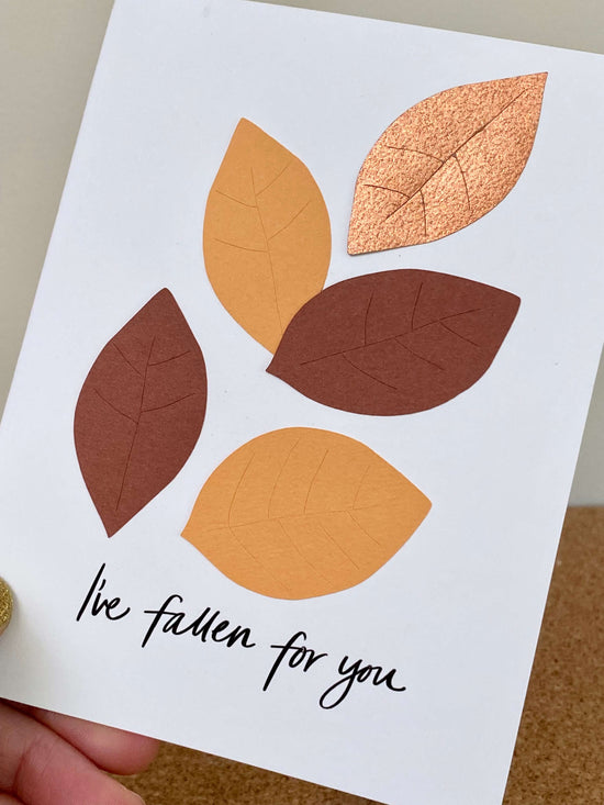 hand holding a white greeting card with five paper leaves in browns and golds, with the text, "I&