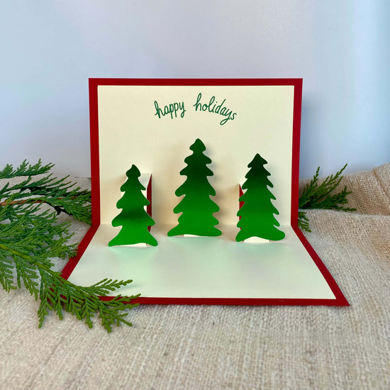 Pop-up holiday card with three green foil trees and a red cover.