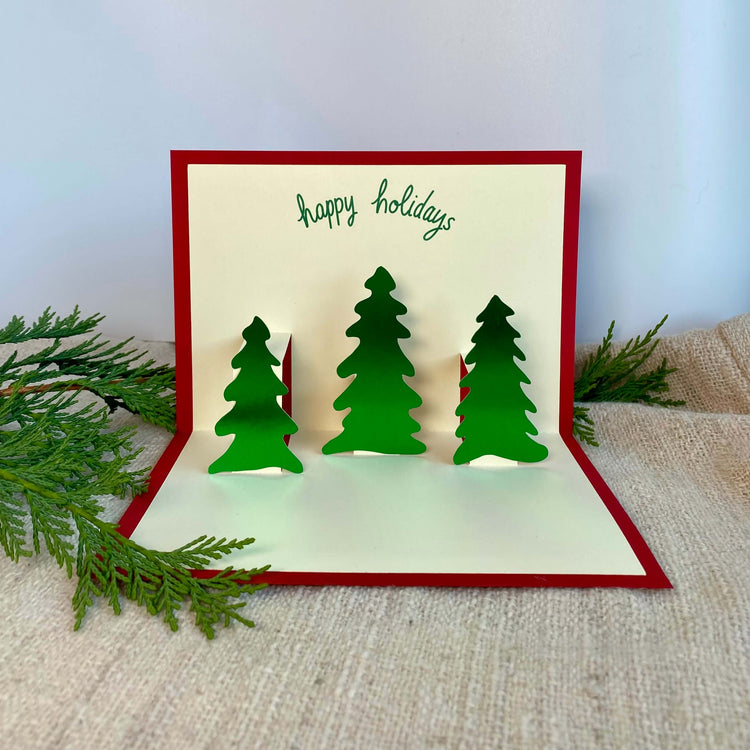 Pop-up holiday card with three green foil trees and a red cover.